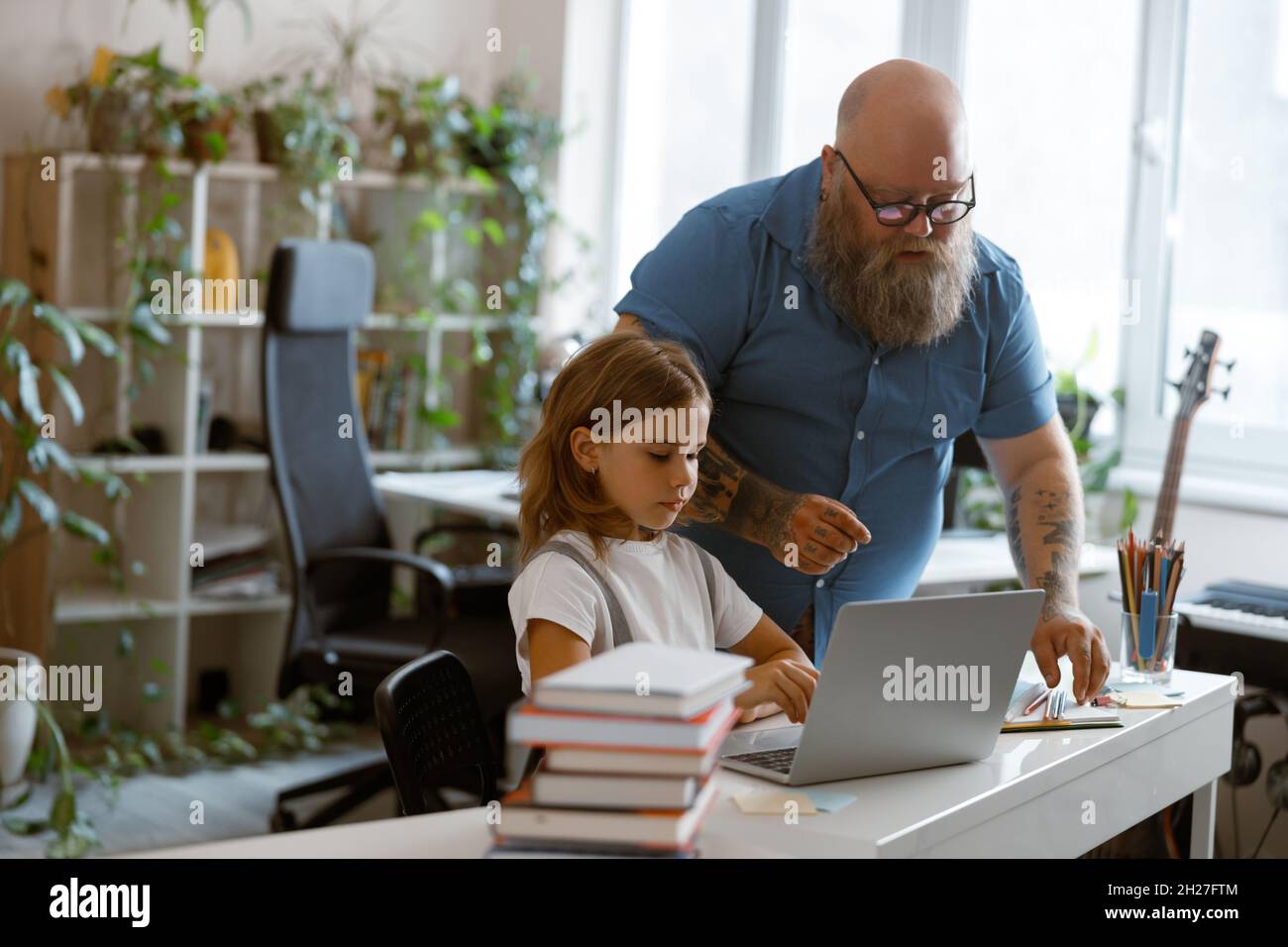 Careful father helps little daughter to prepare to video llesson via laptop at home Stock Photo