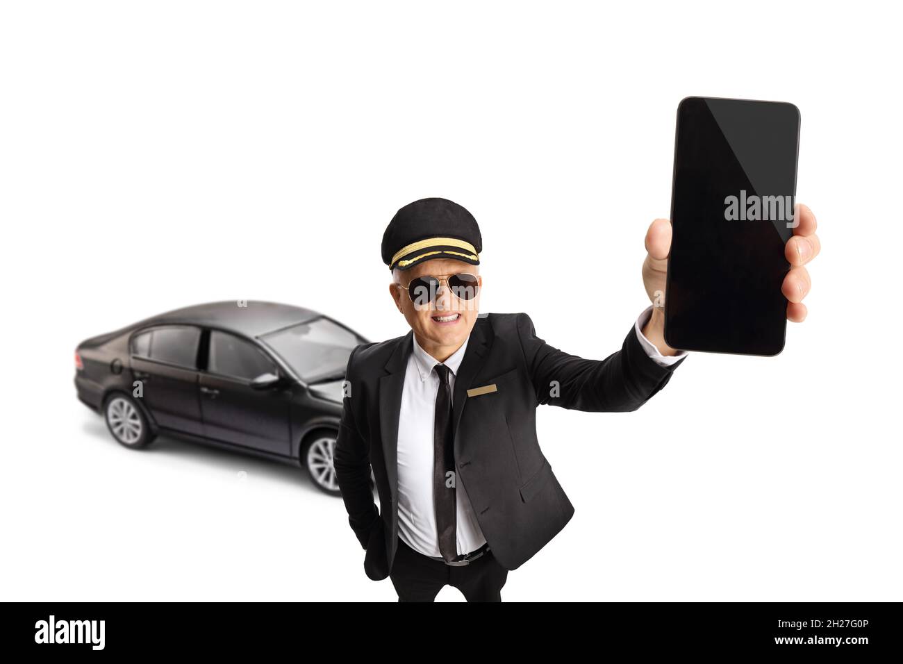 Mature chauffeur in a uniform holding a smartphone in front of a black car isolated on white background Stock Photo