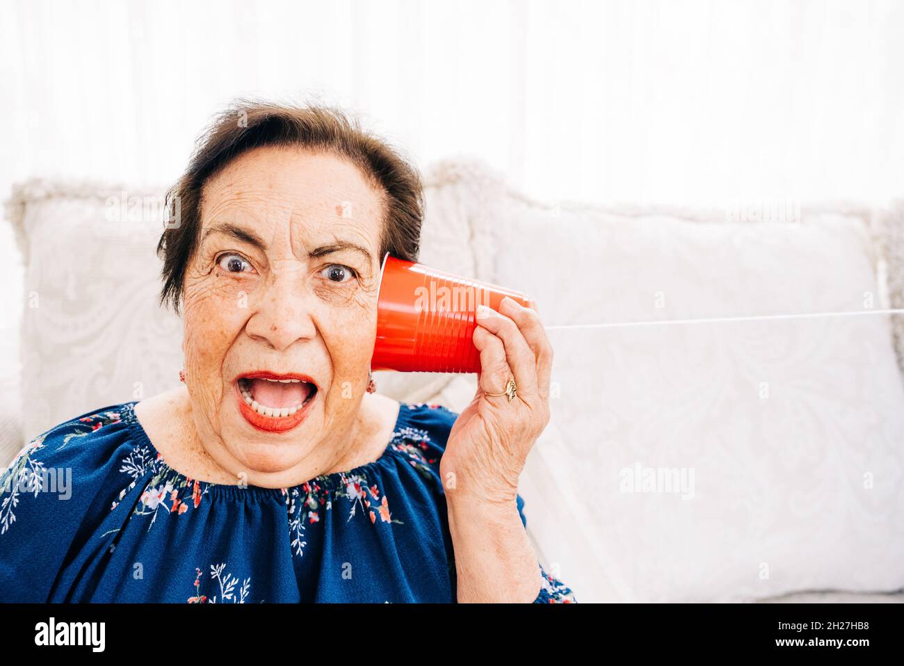 Surprised senior woman listening to a string telephone Stock Photo