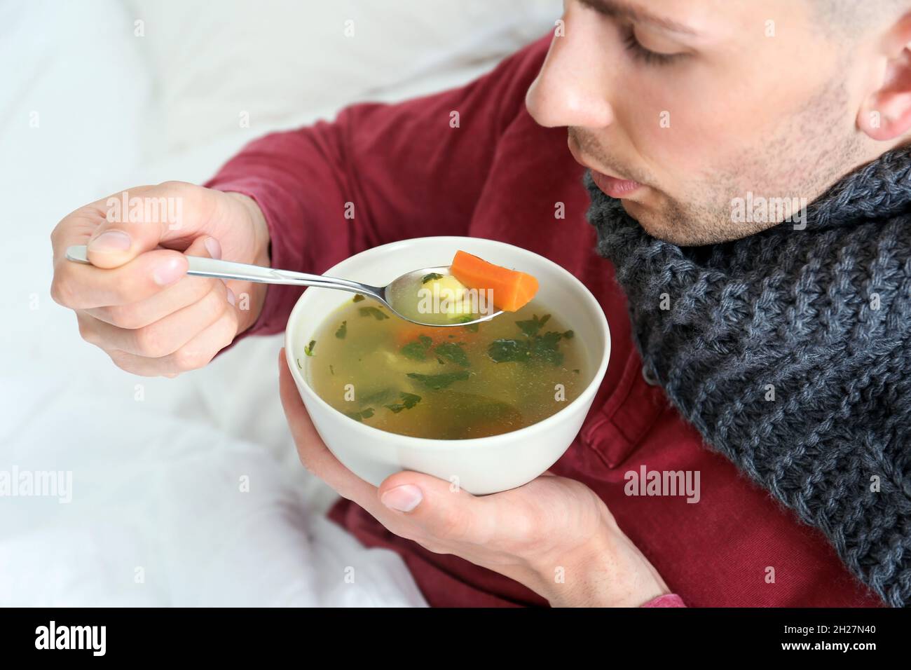 Sick young man eating broth to cure cold in bed at home Stock Photo - Alamy