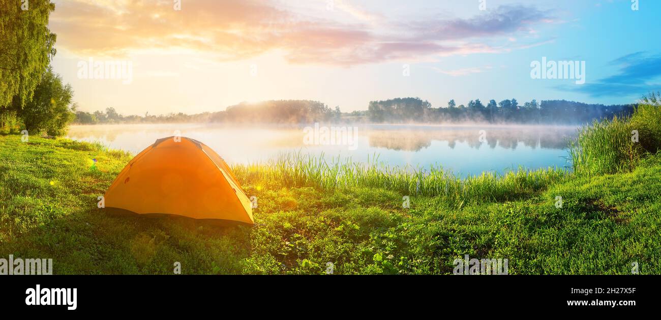 Orange tourist tent in green grass of lake shore Stock Photo