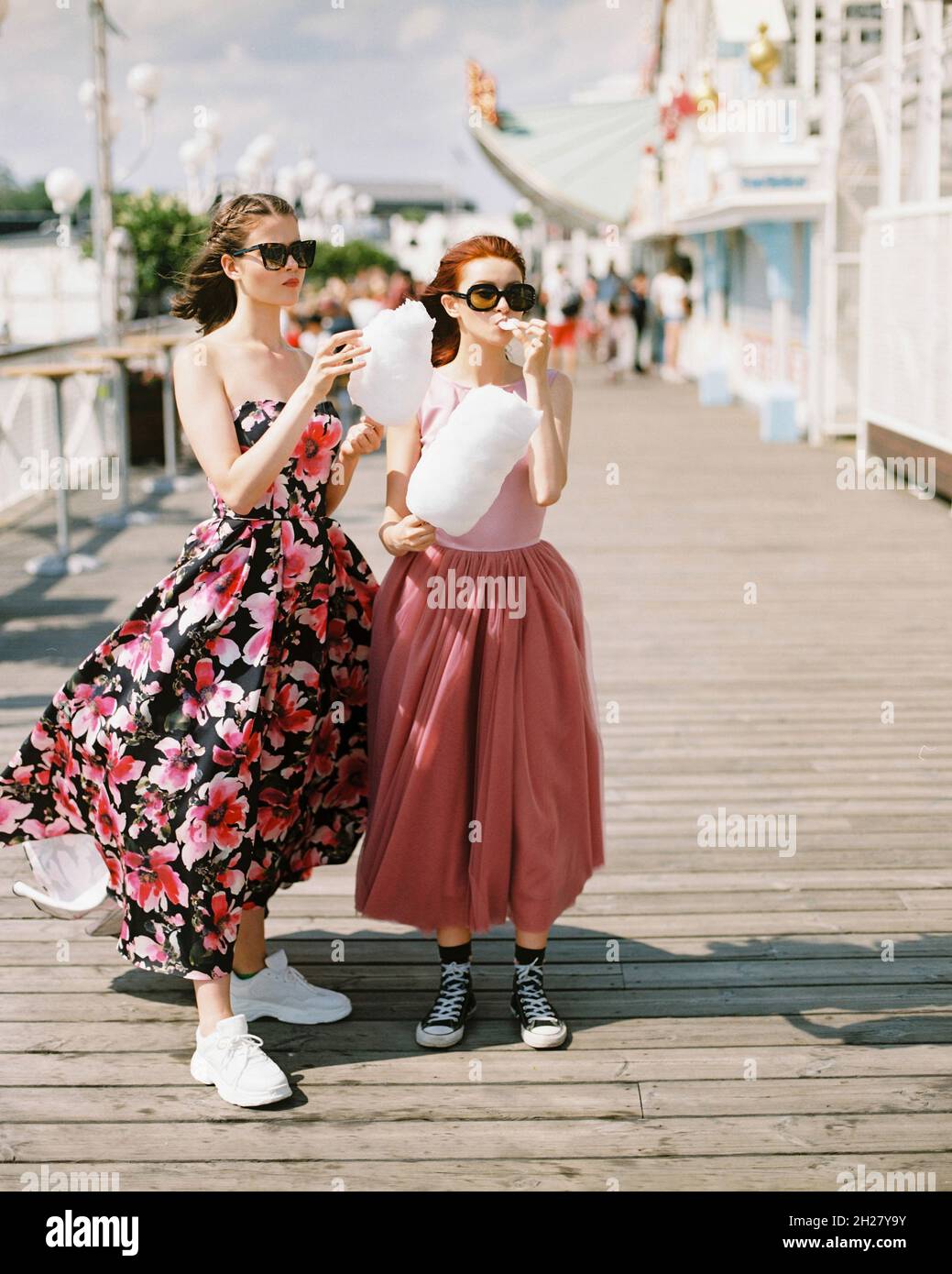 Happy girls with sunglasses and prom dresses eating cotton candy at amusement park. Teenagers in pink evening dresses on vacation. Birthday party idea Stock Photo