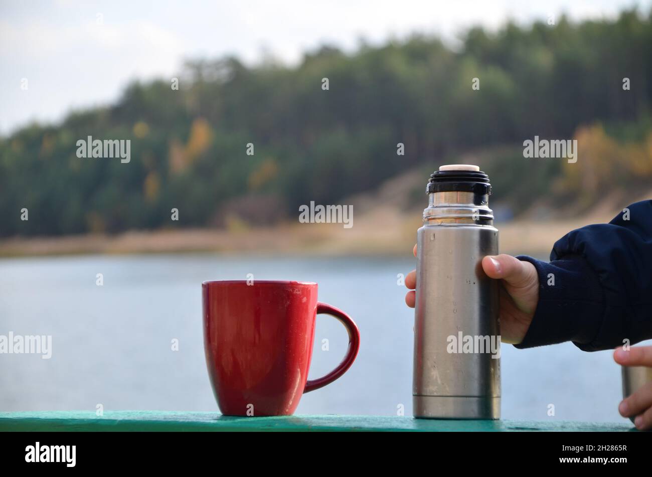 https://c8.alamy.com/comp/2H2865R/the-guy-is-holding-a-black-stylish-eco-friendly-stainless-steel-thermos-and-pours-hot-herbal-tea-into-a-mug-outdoors-on-a-sunny-autumn-day-near-the-l-2H2865R.jpg