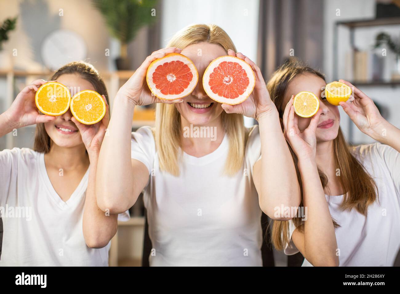 Happy sisters and their charming mother covering eyes under slices of