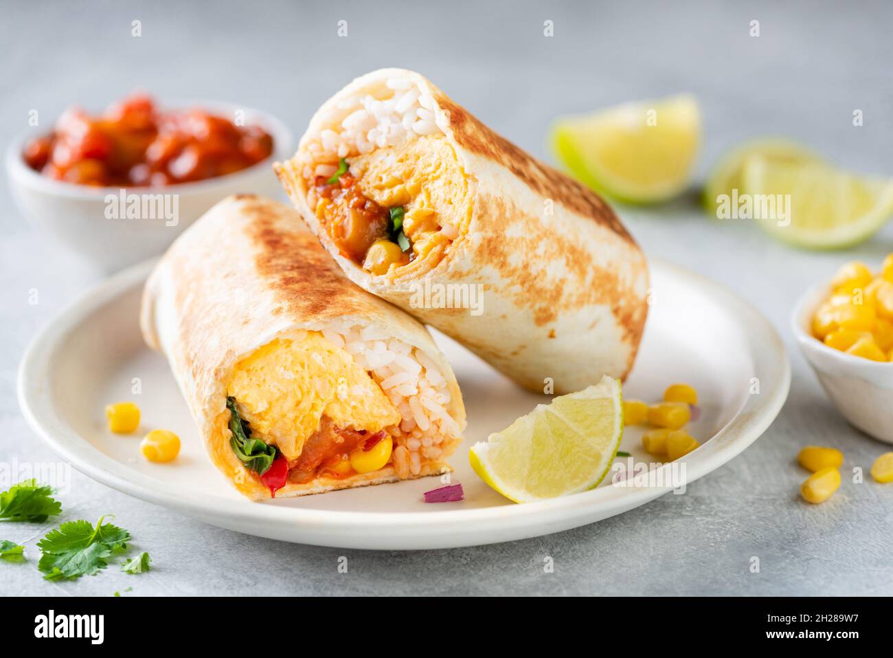 Breakfast vegetarian burrito wrap with omelette and vegetables on a plate. Tortilla wrap sandwich Stock Photo