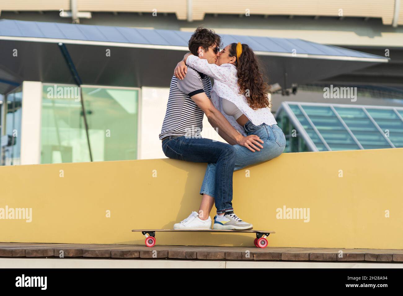 Stylish couple kissing sitting in skatepark. Young cute longboarders man and woman in love cuddling Stock Photo