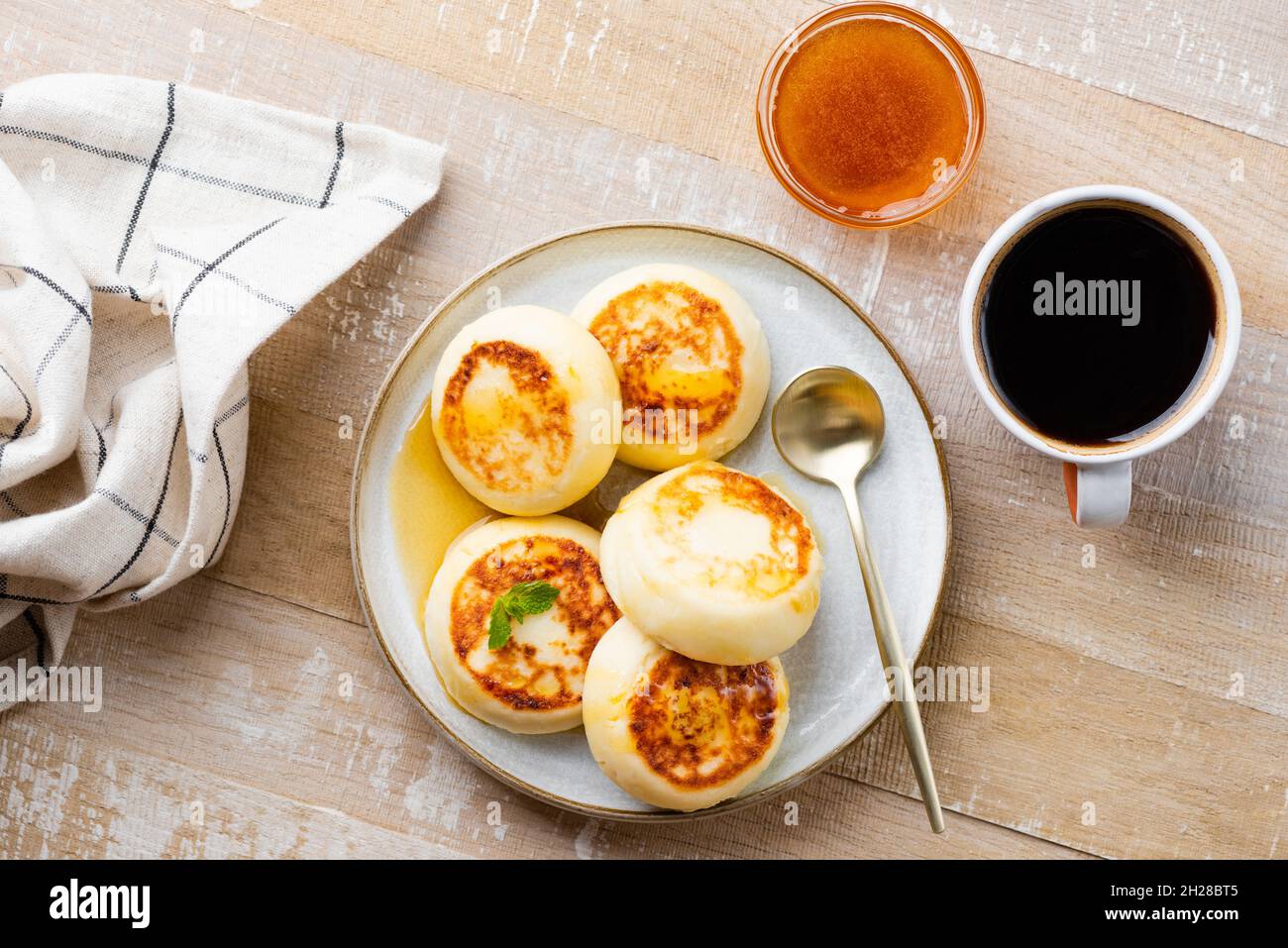 Fried cottage cheese pancakes, fritters or syrniki on a wooden table served with honey and cup of black coffee, top view. Ukrainian, Russian food Stock Photo