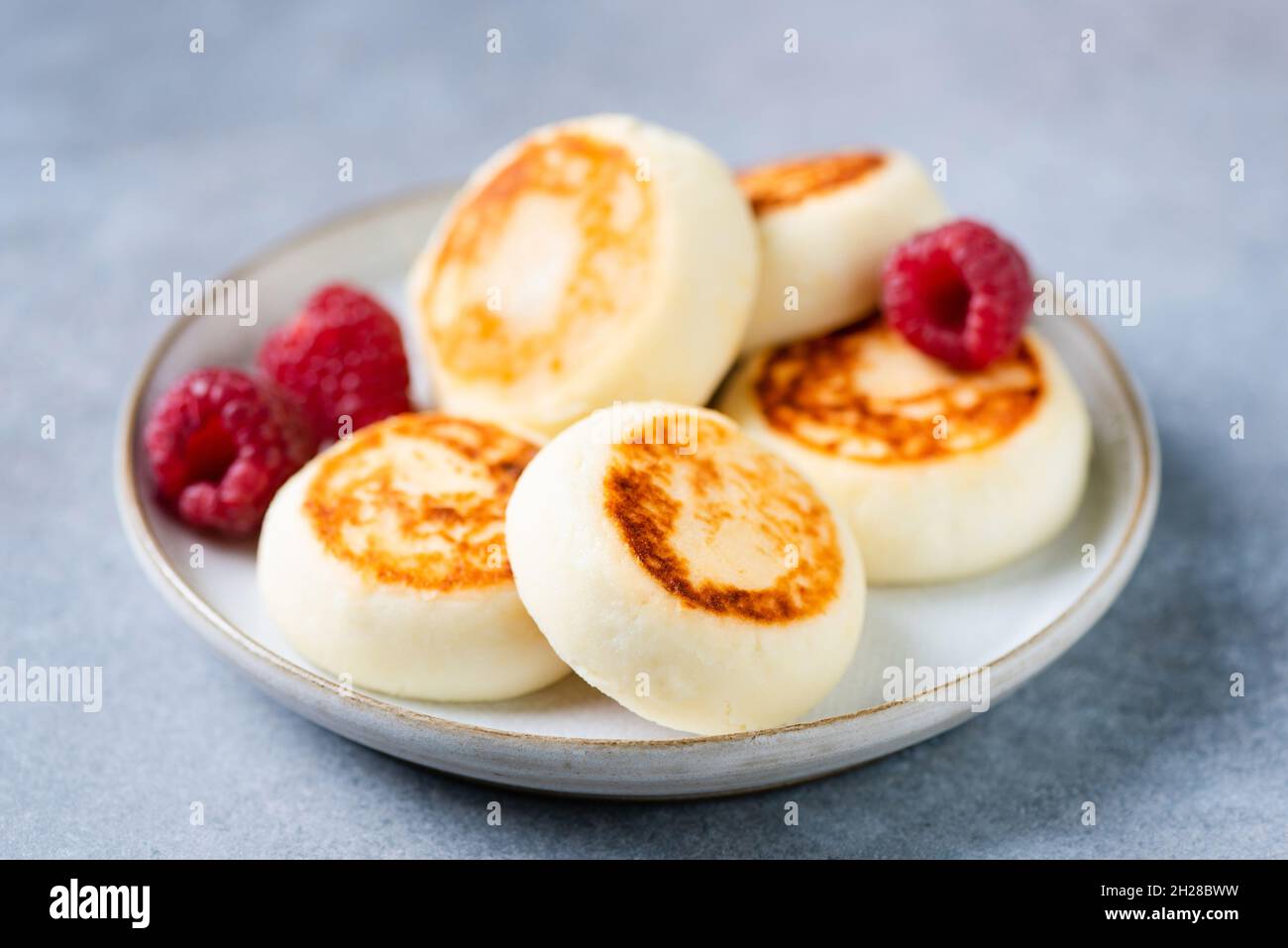 Cottage cheese fritters with raspberries isolated on blue concrete background, closeup view Stock Photo