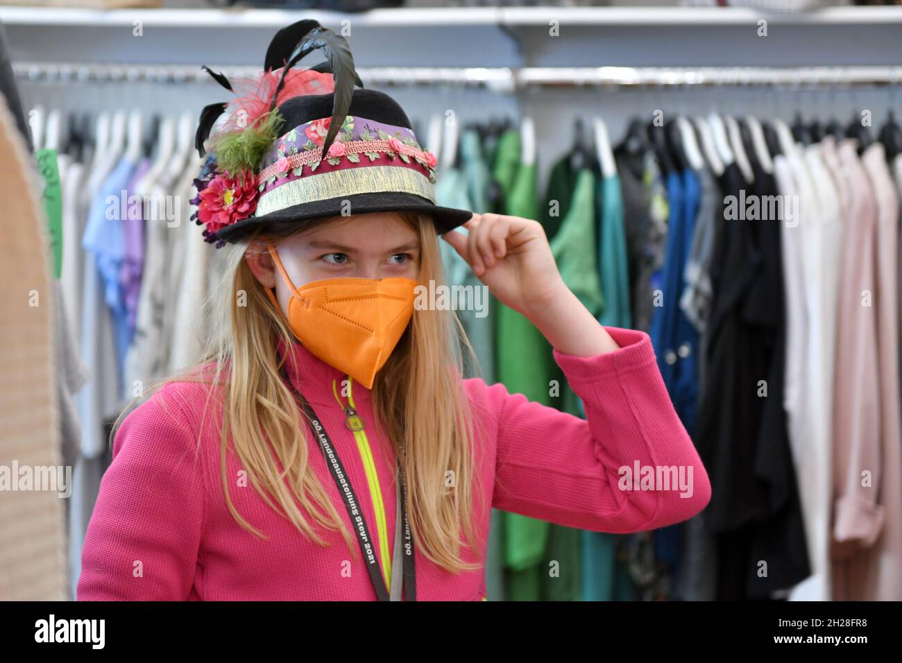 Mädchen mit Hut und oranger FFP2-Maske in einem Kleidergeschäft in Steyr, Österreich, Europa - Girl with hat and orange FFP2 mask in a clothes shop in Stock Photo