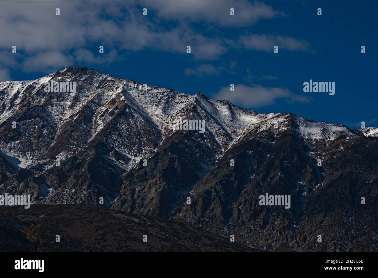 Snow capped Sierra Nevada mountains, showcasing ridgeline & defining its texture, changing patterns & shape.  Rich blue skies with lofty clouds. Stock Photo