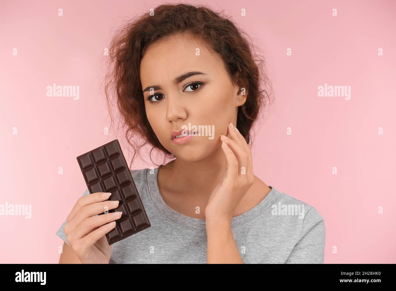 Beautiful young woman with acne problem holding chocolate on color