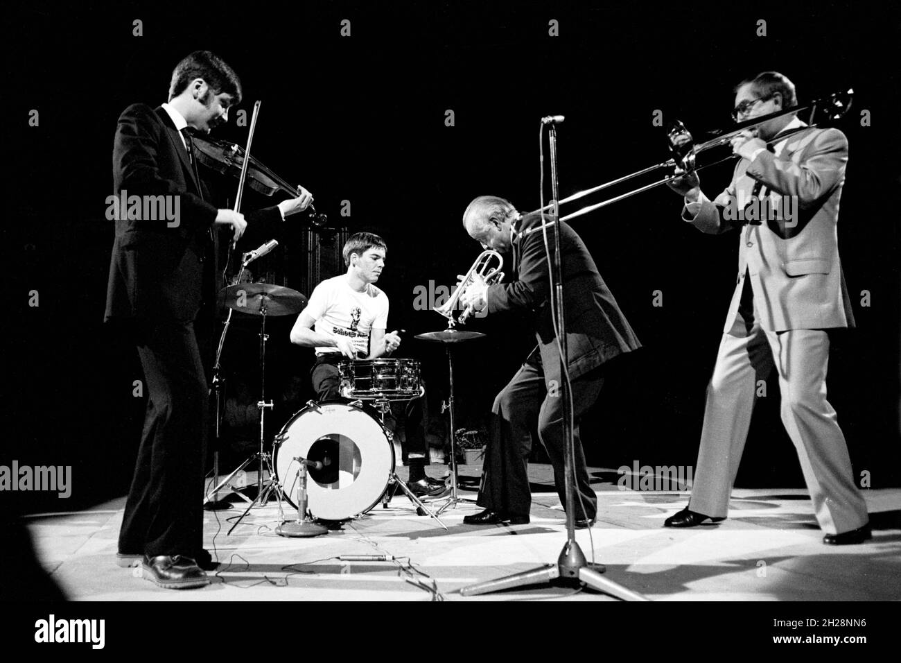 Violinist Nigel Kennedy, aged 26, jamming with trumpeter Kenny Baker, trombonist Don Lusher, OBE and a young member of the Doncaster Jazz Orchestra at one of the Schools Prom concerts, Royal Albert Hall, London, England in 1982. Stock Photo