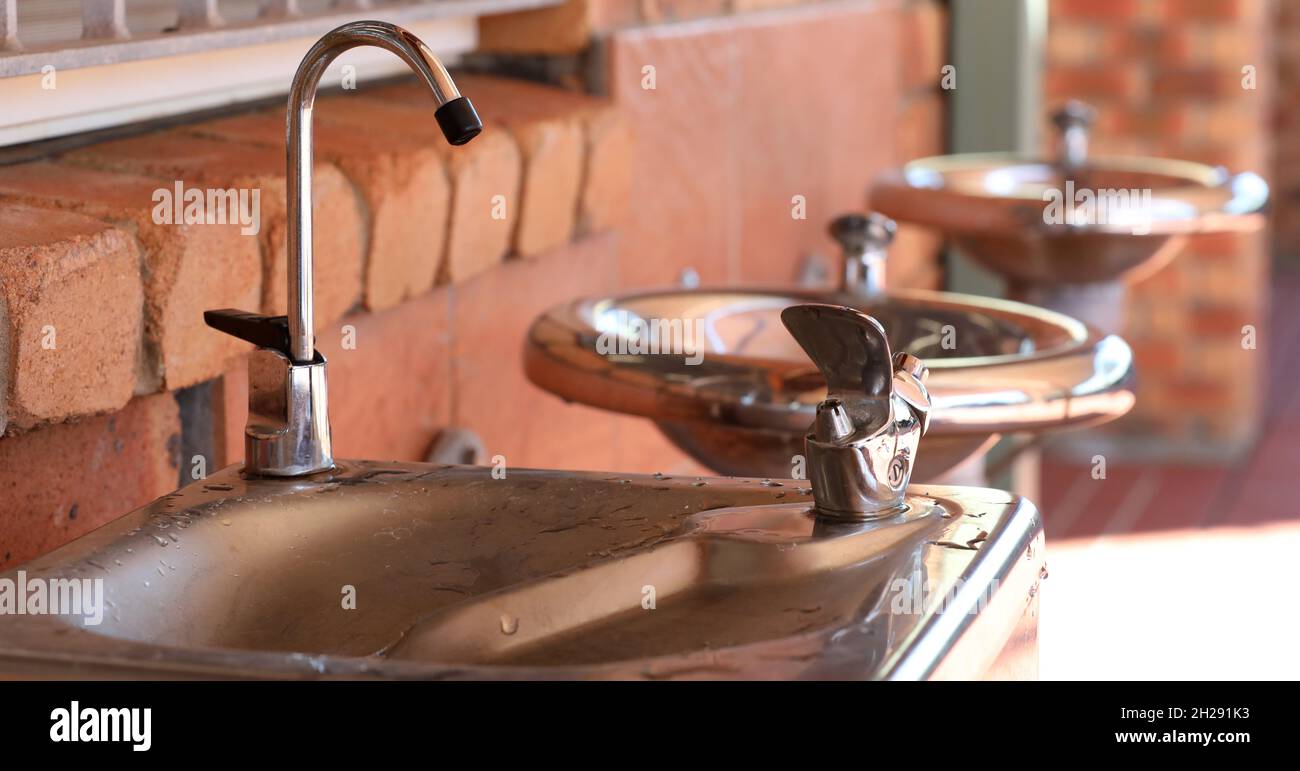 A row of three stainless steel fresh water bubblers or fountains. Chilled spring filtered water tap in foreground. Access to safe water supply or acce Stock Photo