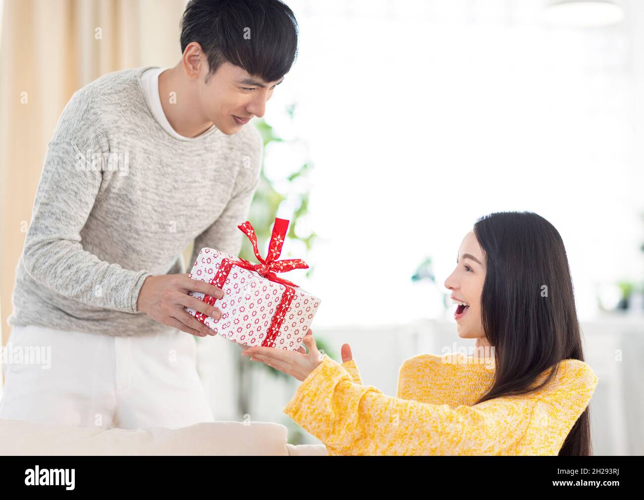 Young couple giving the gift box in living room Stock Photo
