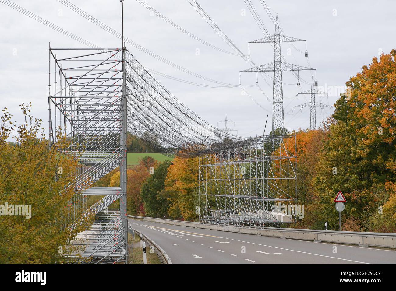 A large scaffolding with a safety net to protect road traffic because of work on a high-voltage line and the electricity pylons. Stock Photo