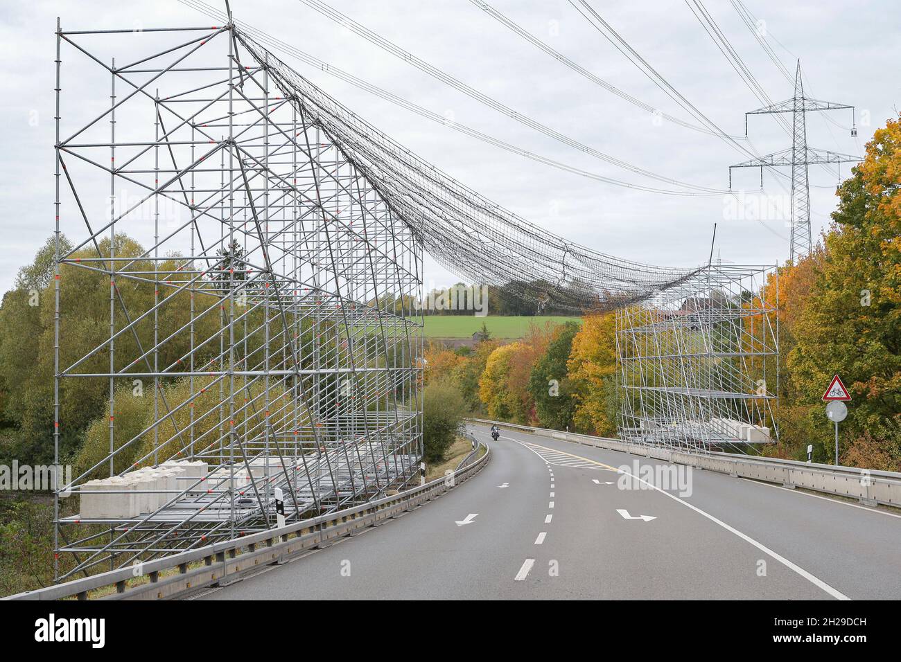 A large scaffolding with safety net to protect the road traffic due to work on a high-voltage line and the power poles. Stock Photo