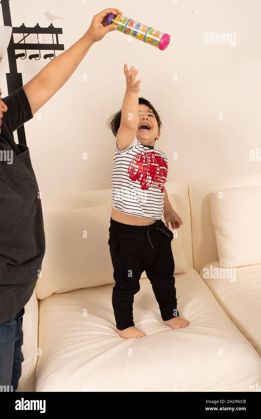 2 year old toddler boy laughing as he reaches for toy parent is holding out of his reach Stock Photo