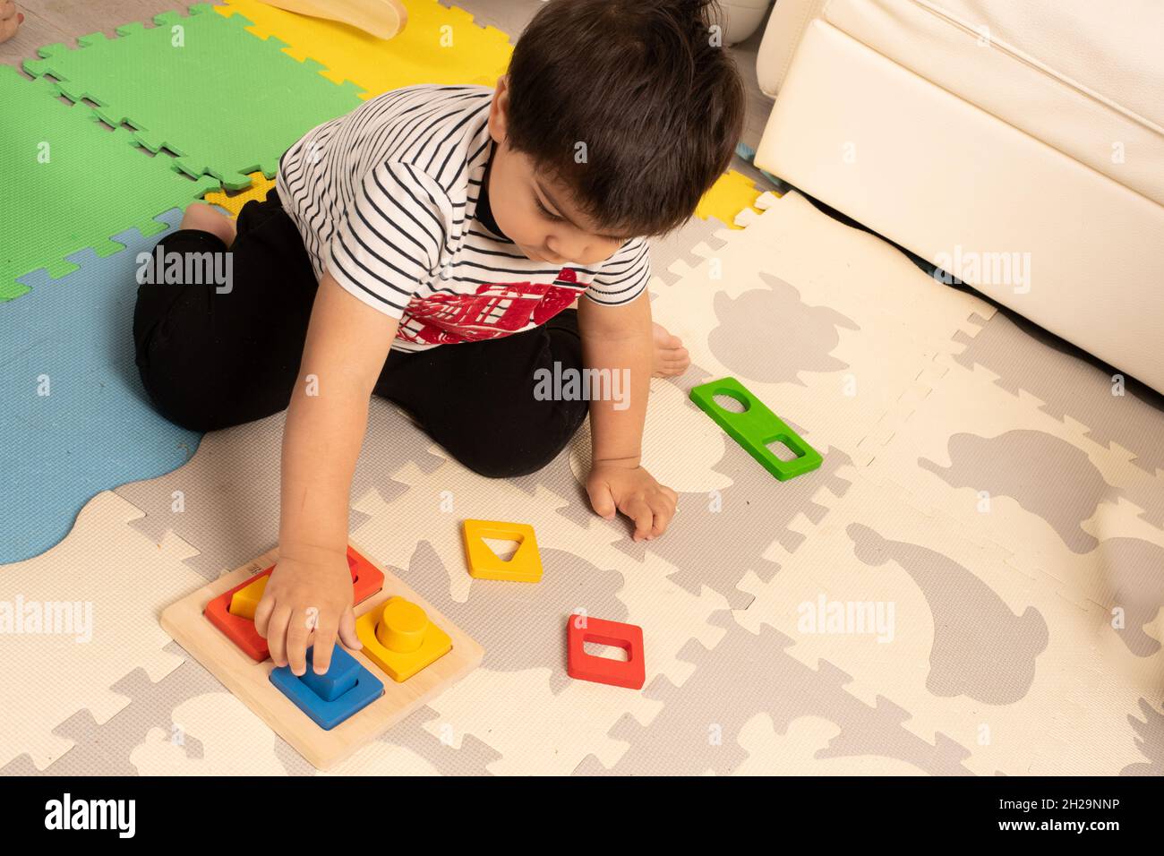 Two year old toddler boy playing with shape sorter puzzle, matching clolors Stock Photo