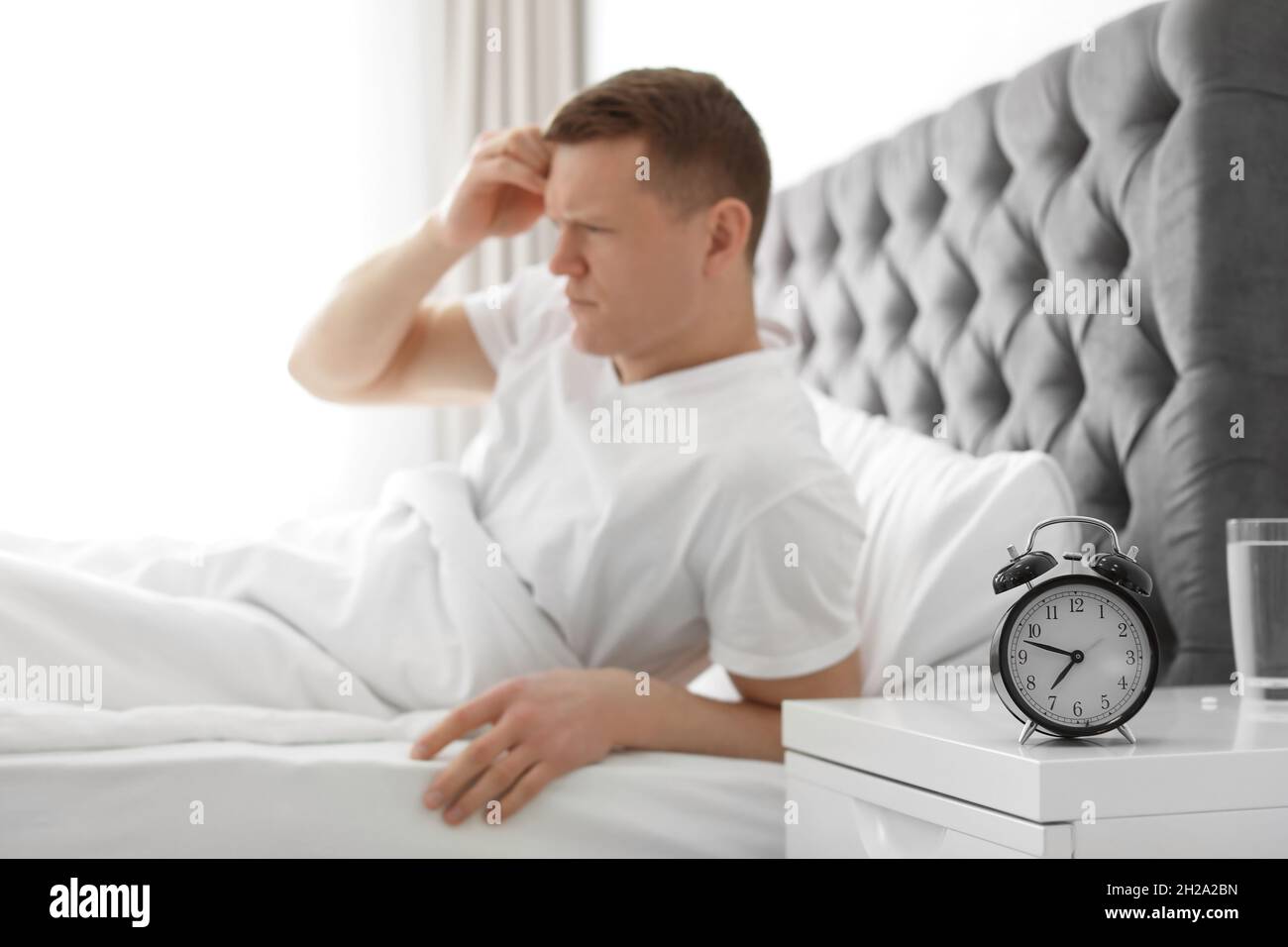 Alarm clock on nightstand of young man suffering from headache Stock