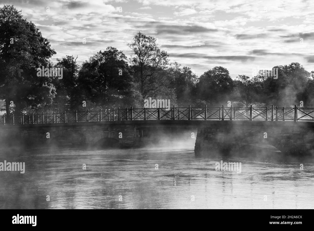 Misty morning, grayscale photography of bridge, lake and mist. Stock Photo