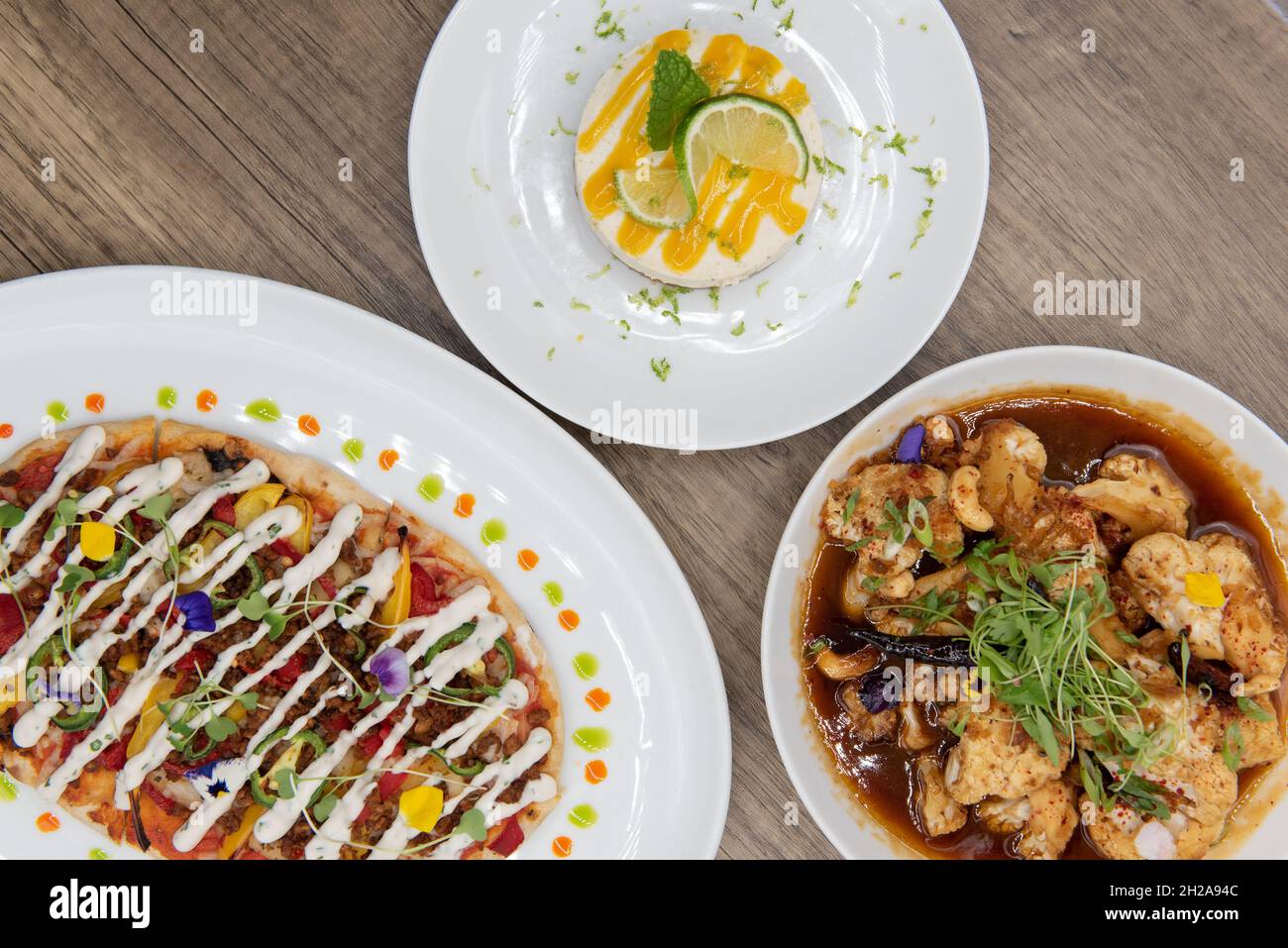 Overhead view of hearty table of flat bread pizza, key lime pie, and tangy roasted cauliflower on a wooden surface. Stock Photo