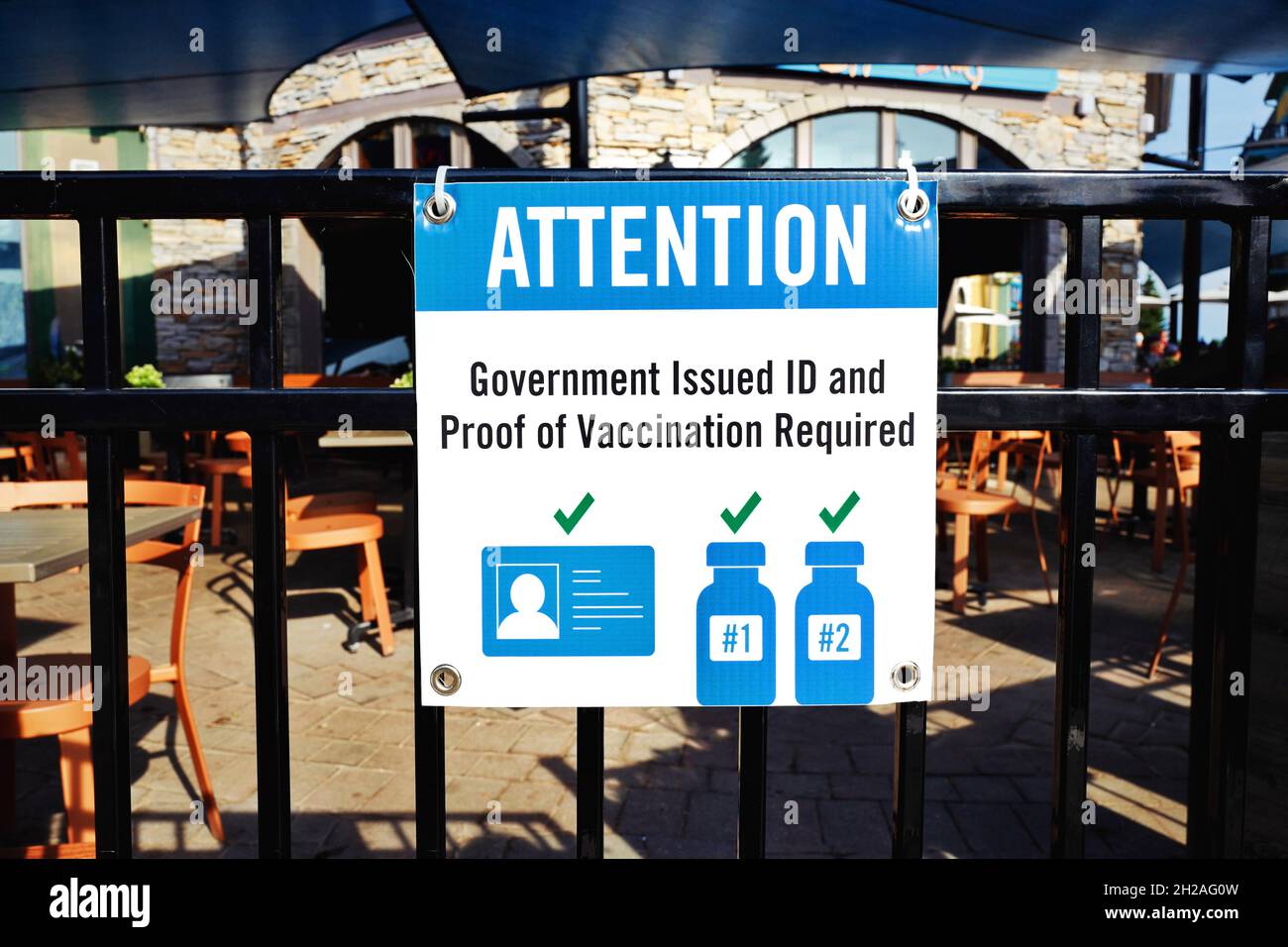 Government issued ID and proof of vaccination required sign against blurred restaurant entry and patio seats. Proof of COVID-19 vaccination two doses. Stock Photo