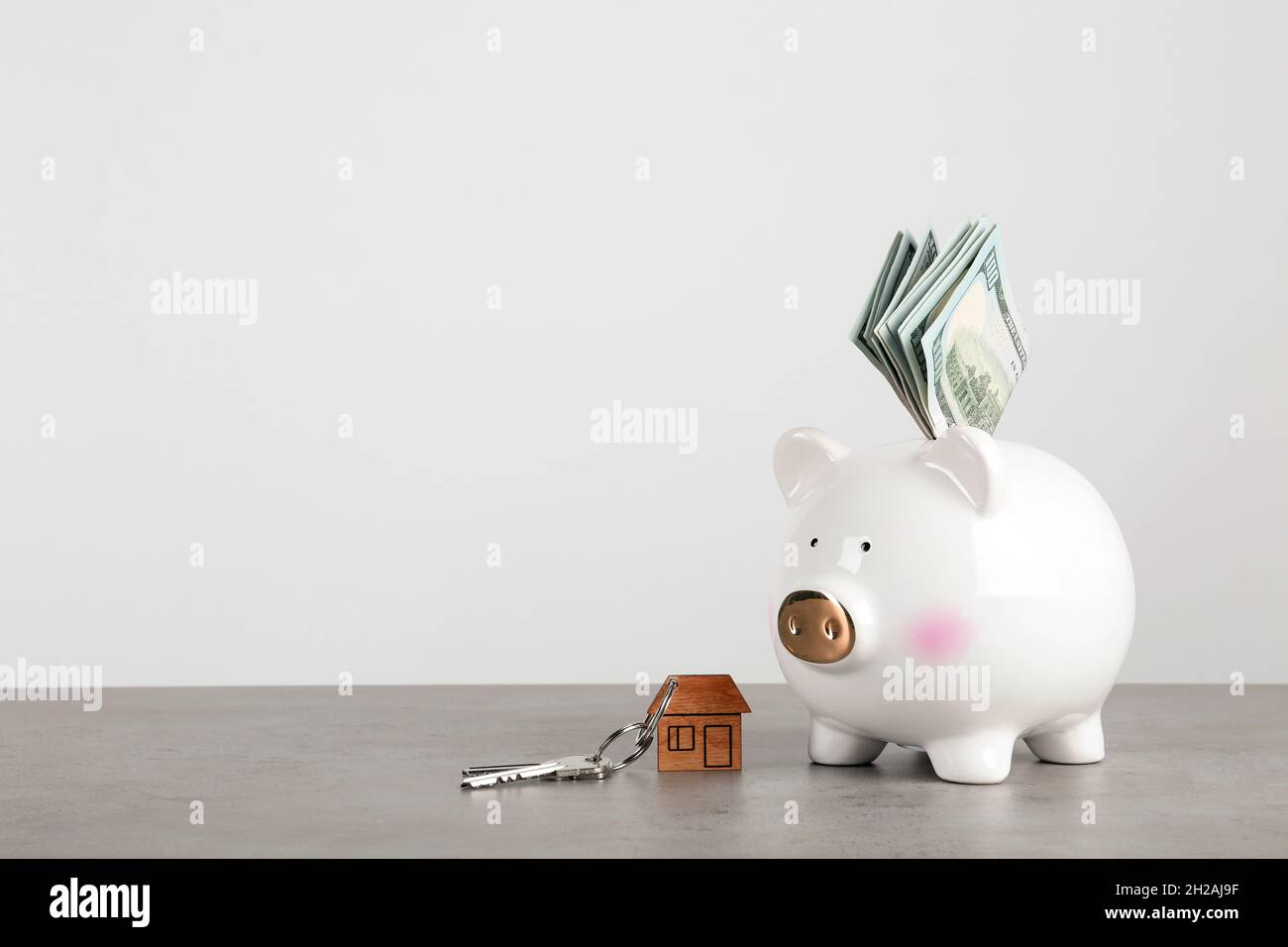 Piggy bank with dollar banknotes and house keys on table against white ...