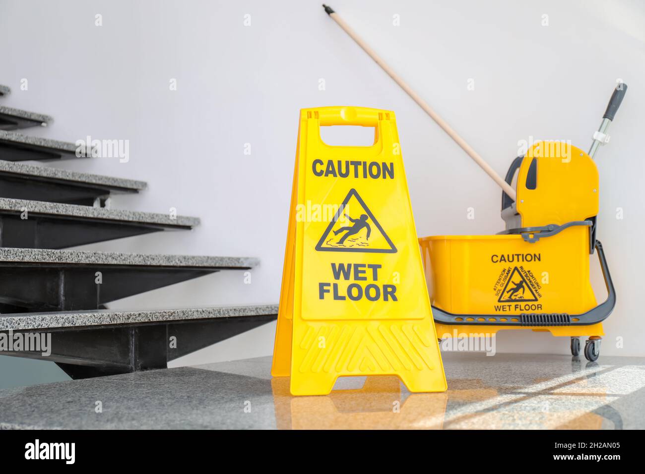 https://c8.alamy.com/comp/2H2AN05/safety-sign-with-phrase-caution-wet-floor-and-mop-bucket-near-stairs-cleaning-service-2H2AN05.jpg