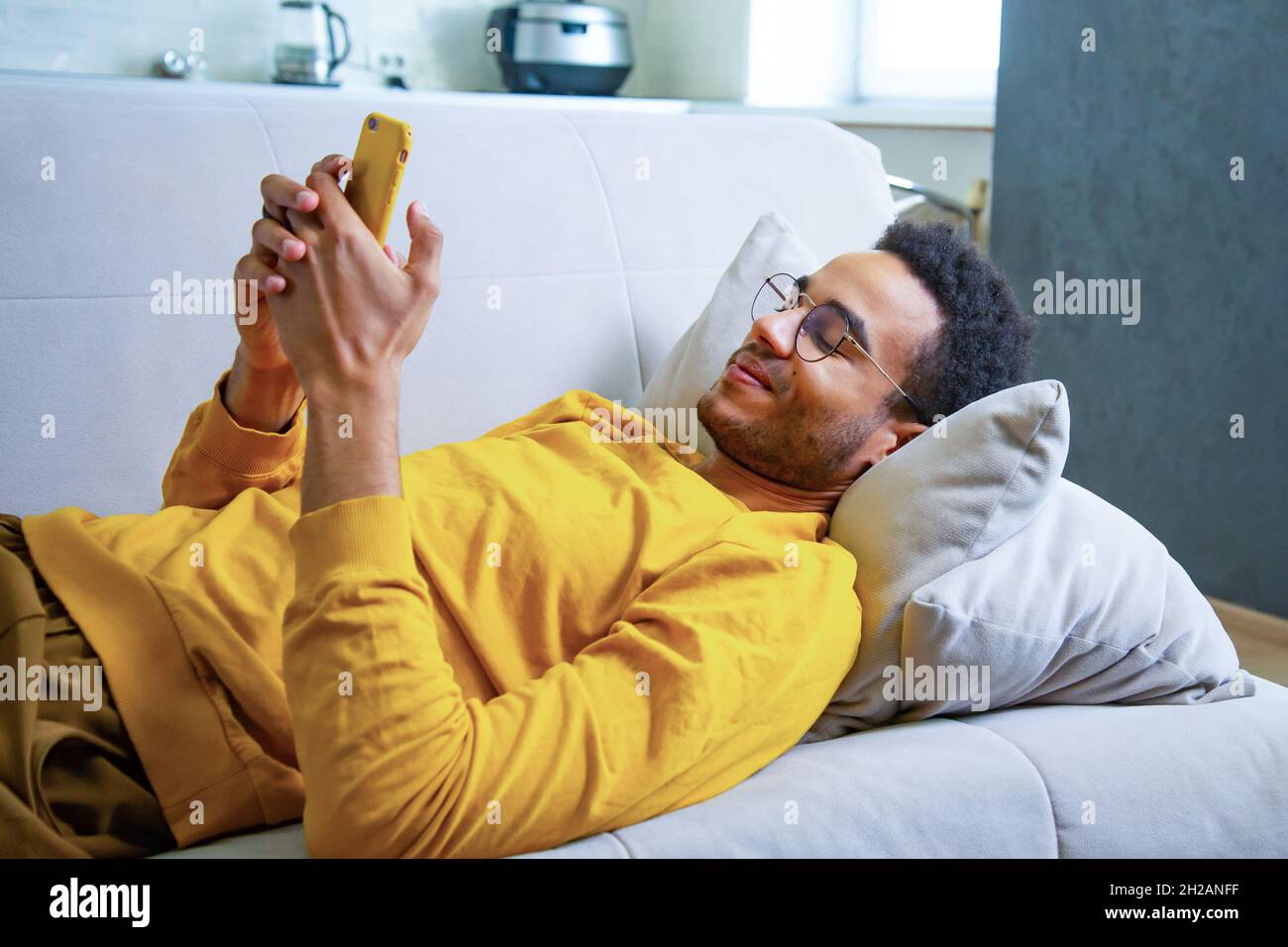 Young African Lying on the Couch Using a Smartphone Stock Photo