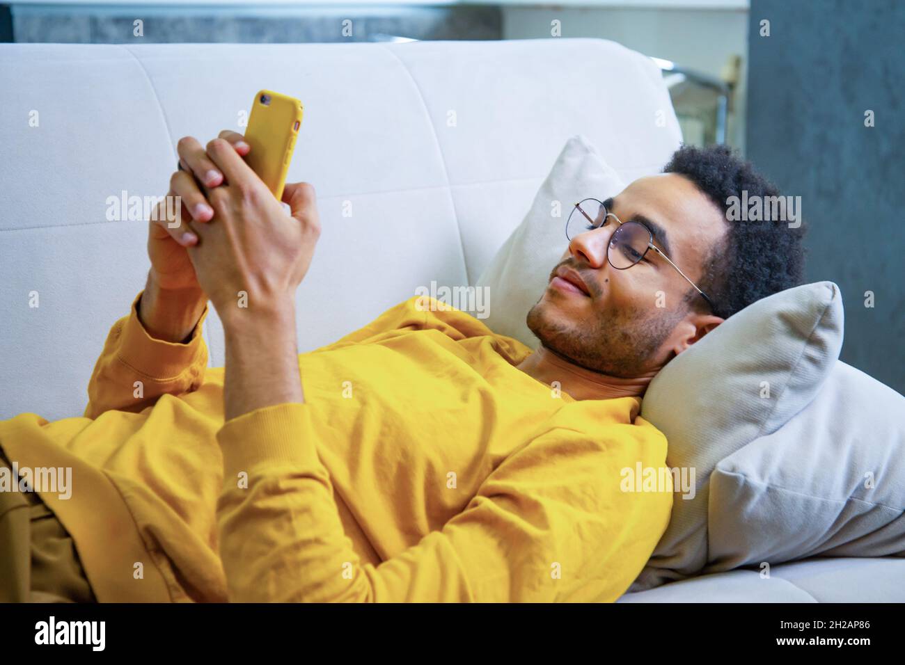 Young African Lying on the Couch Using a Smartphone Stock Photo