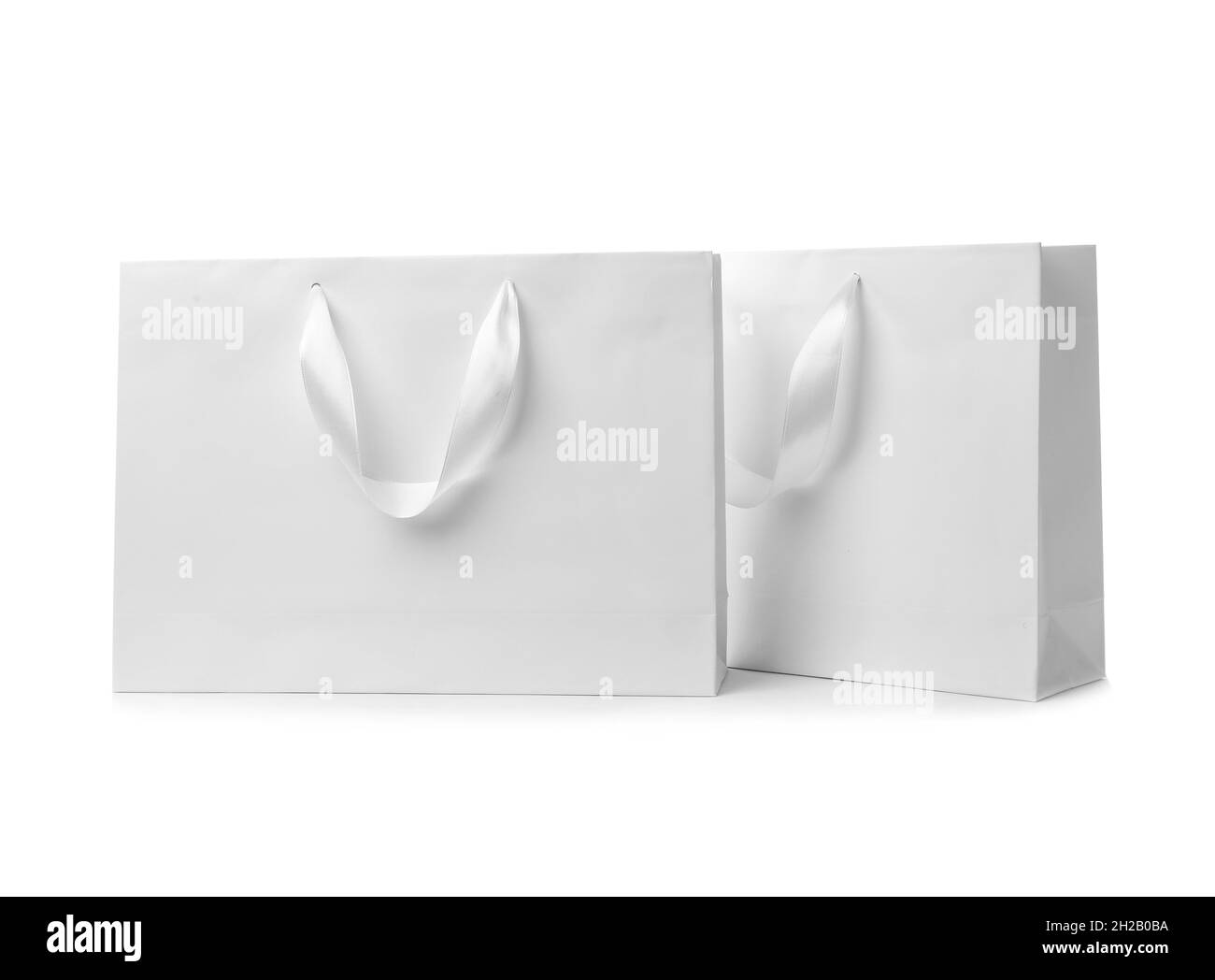 Paper shopping bags with ribbon handles on white background. Mockup for