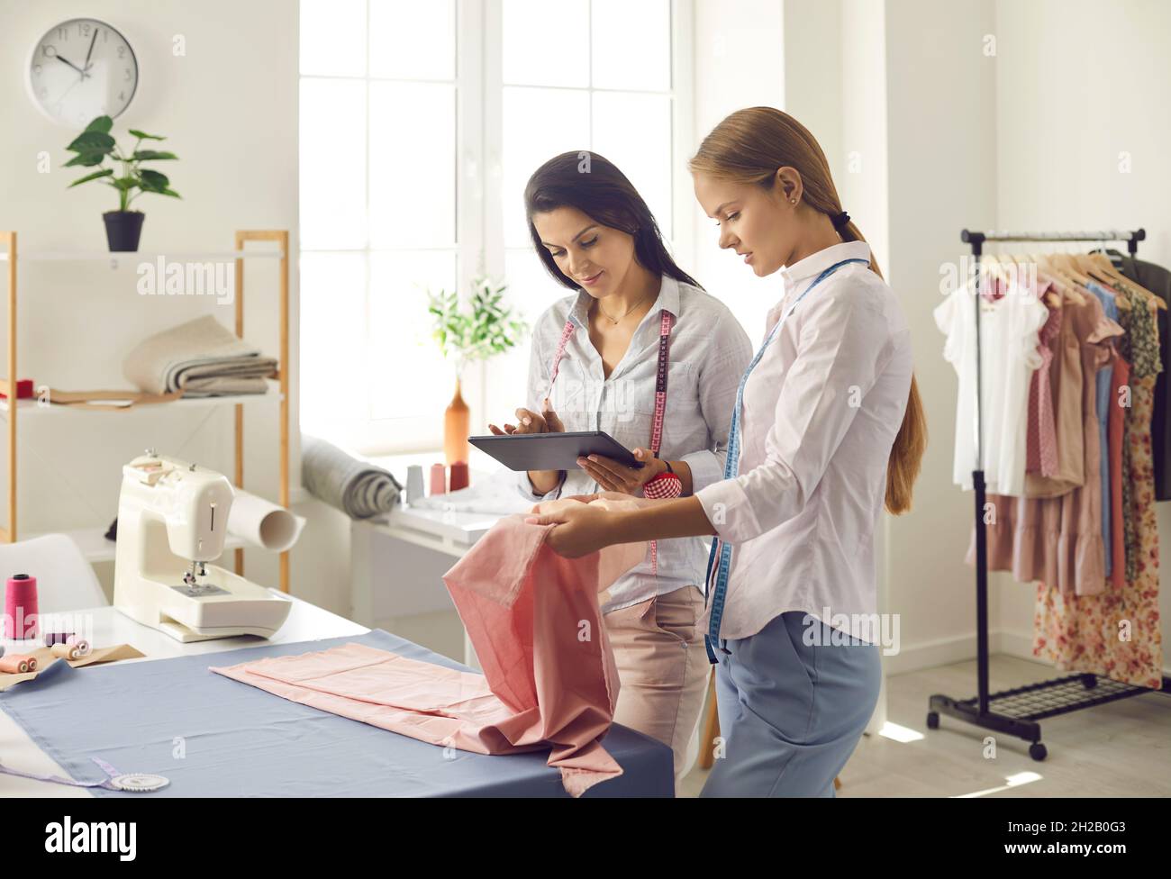 Two female atelier owners check catalog with new fabric samples on digital tablet. Stock Photo