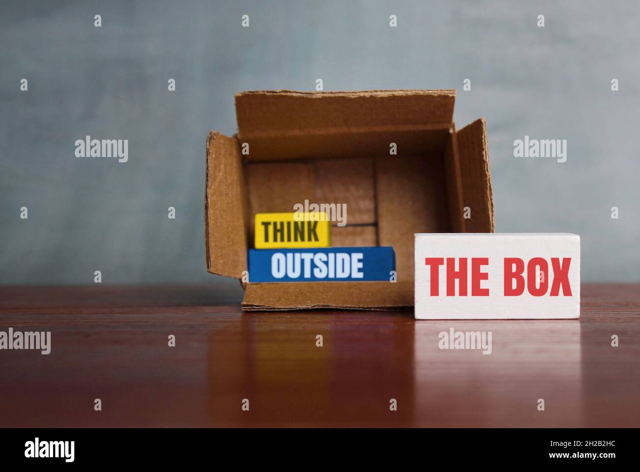 Think differently, unconventionally, or a new perspective concept. Box and wooden cube with text THINK OUTSIDE THE BOX Stock Photo