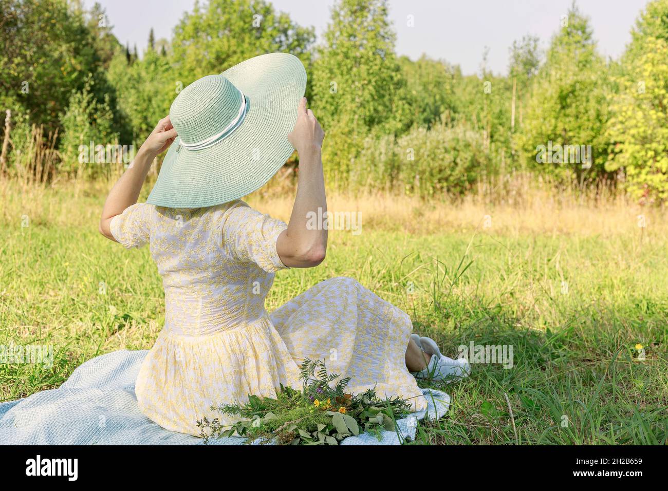Young attractive caucasian woman in a fashionable dress and a big straw hat. Happy lady in summer light dress is enjoying a summer day on the sunny la Stock Photo
