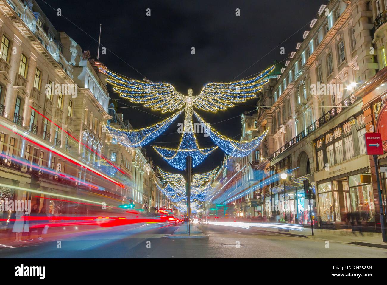 Christmas angel decorations hanging over Regent Street in central London.  Long exposure creating light trails from cars and buses. Stock Photo