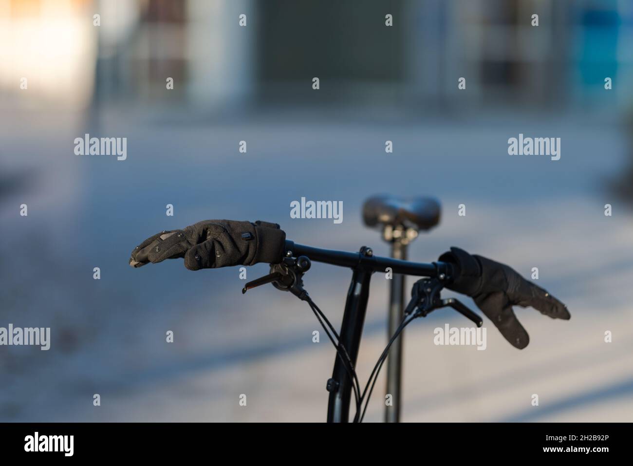 Black pair of modern synthetic gloves stuck on handlebar of folding bike standing in suburban area with blurred background on cold sunny winter mornin Stock Photo