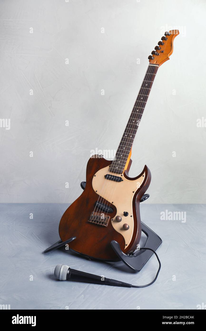 Stand with modern electric guitar and microphone on floor near color