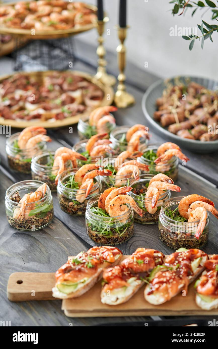 Delicious fresh seafood, shrimp with fresh vegetables. buffet table with lots of delicious snacks. canapes, bruschetta, and little desserts on wooden Stock Photo