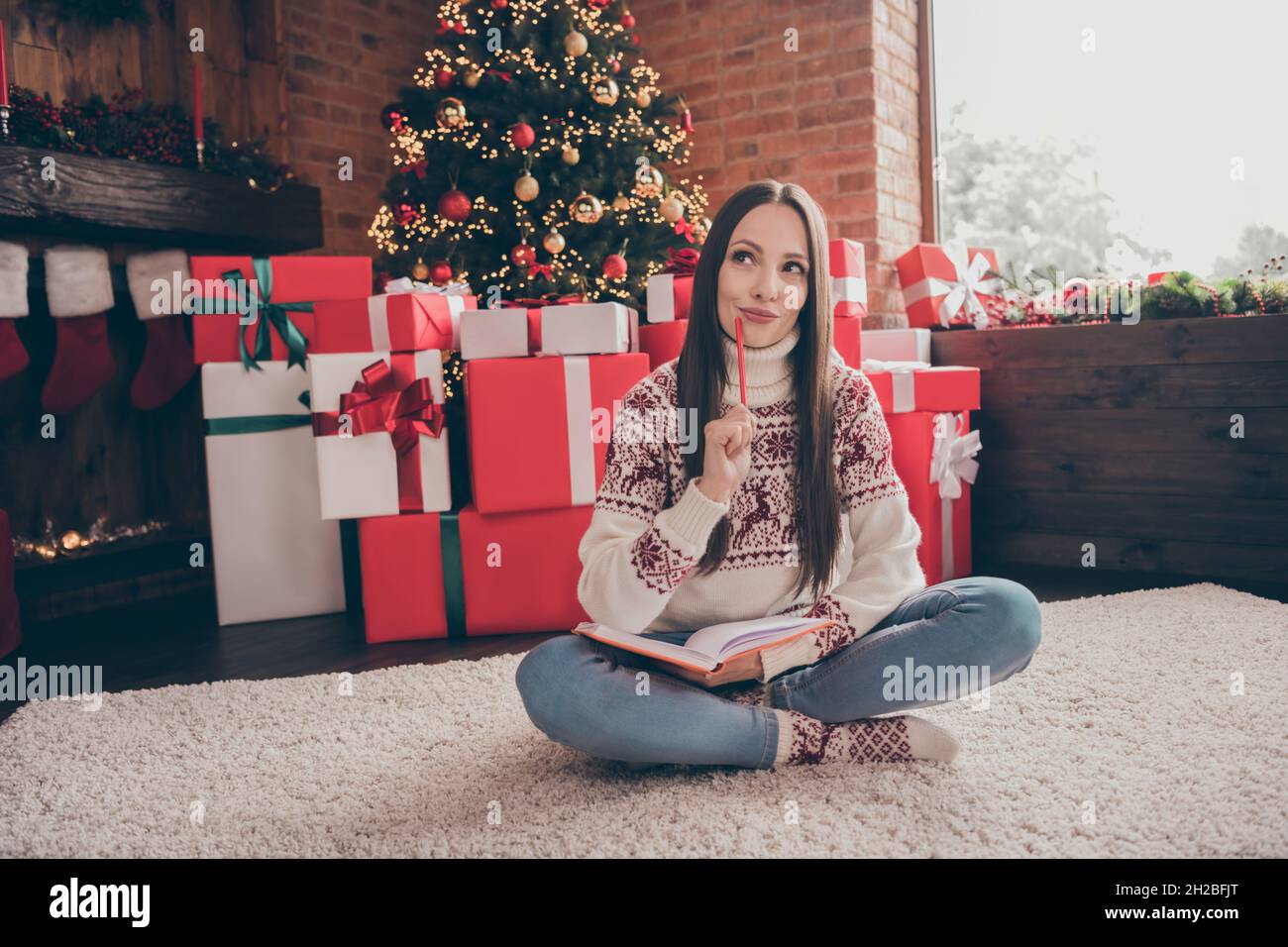 Full size photo of dream young lady write list sit near present tree wear sweater jeans socks christmas at home Stock Photo