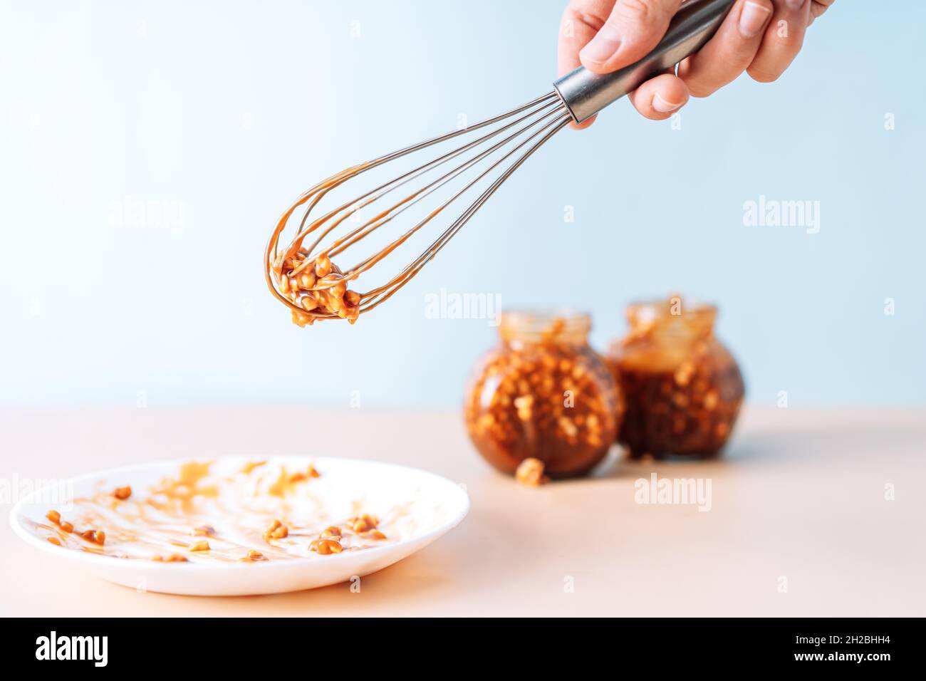 Plate and metal whisk in caramel opposite glass jars Stock Photo Alamy