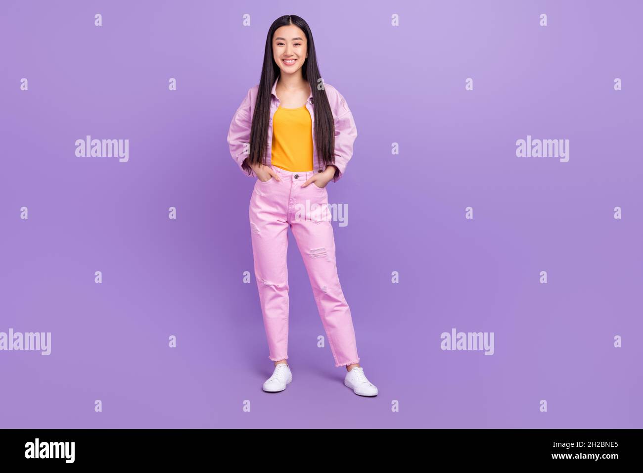 Full length photo of nice young brunette lady wear pink jacket jeans sneakers isolated on violet background Stock Photo