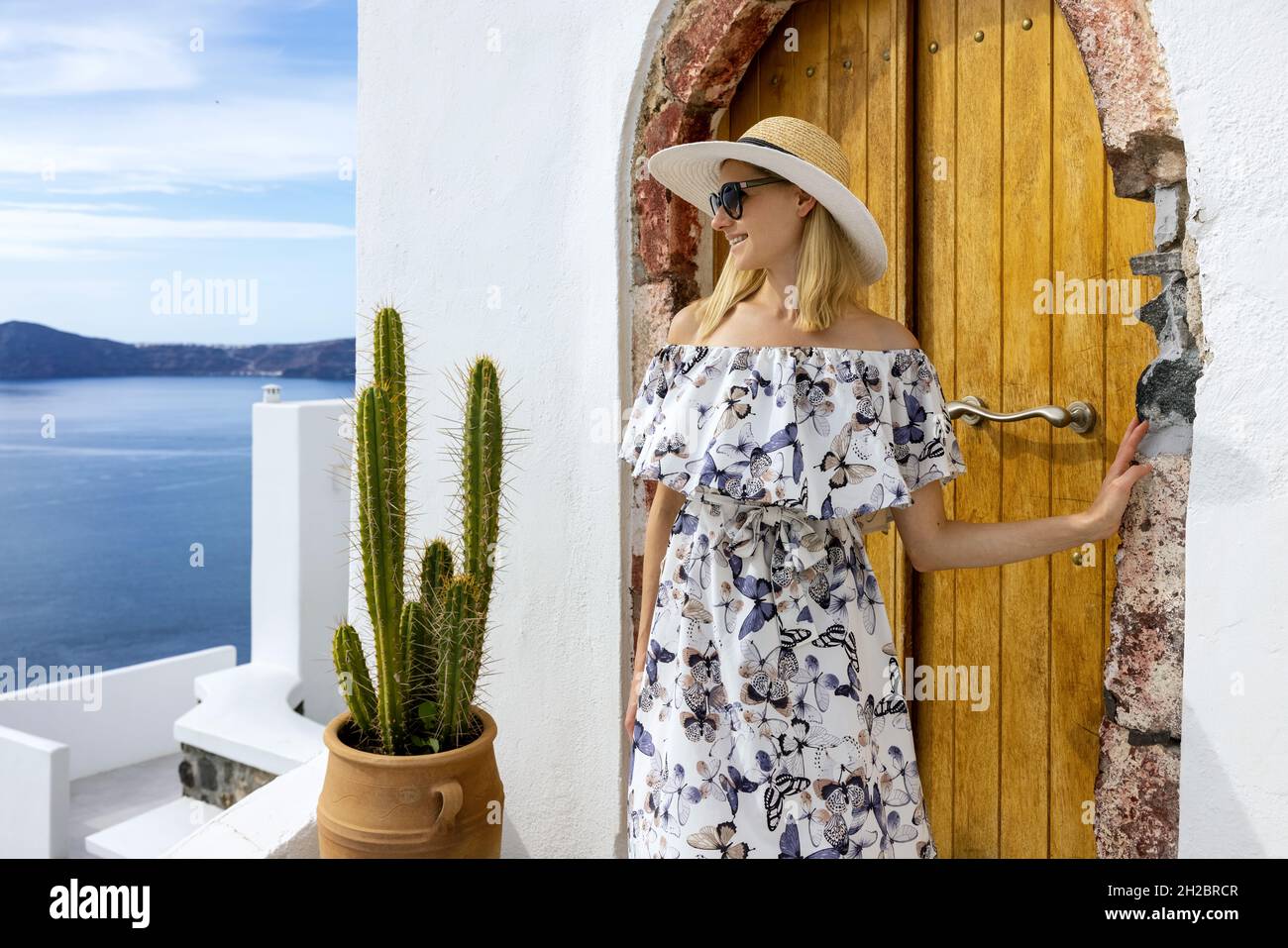 happy young woman in elegant dress and hat on Santorini island streets on sunny summer day Stock Photo