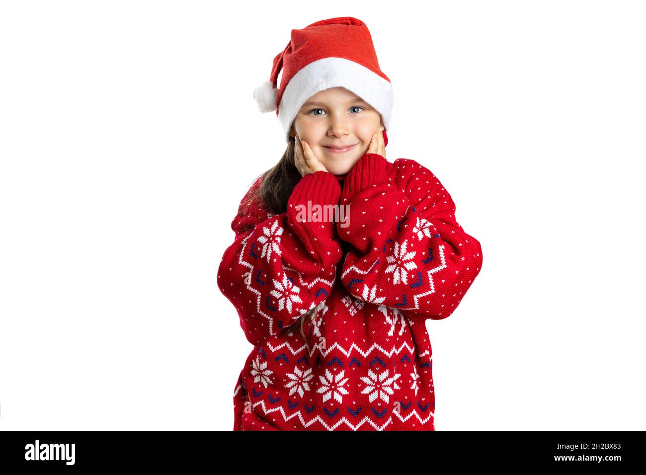 portrait of smiling, cute girl in red Christmas sweater with reindeer touching face with palms, isolated on white background Stock Photo