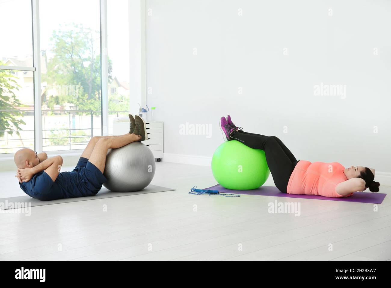 Overweight man and woman doing exercise with fitness balls in gym Stock