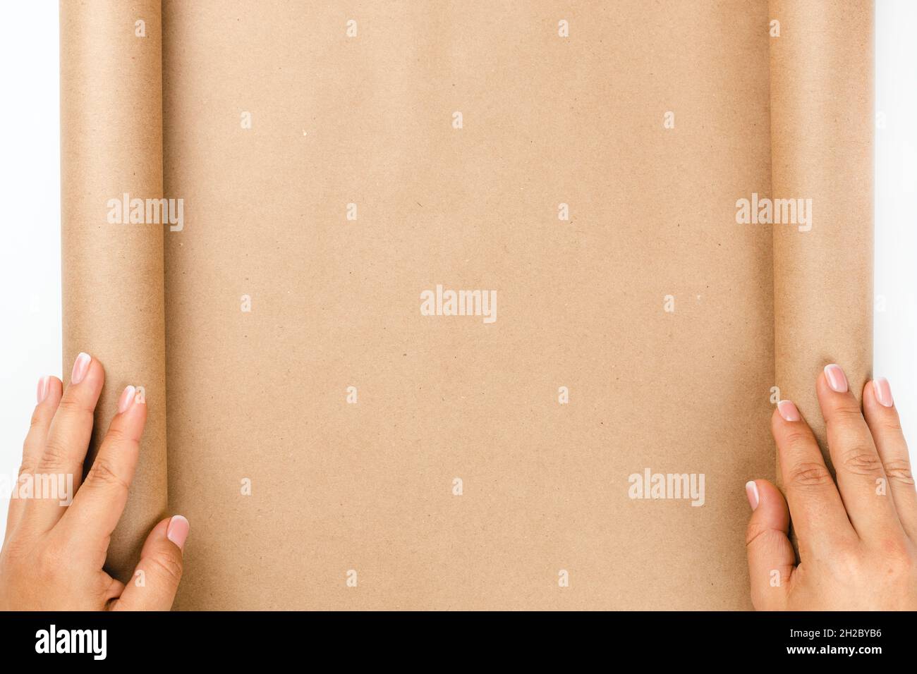 flat lay of two female hands unfolding empty craft paper from roll, background for text Stock Photo