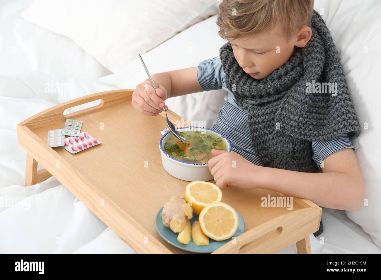 Sick little boy eating broth to cure cold in bed at home Stock Photo