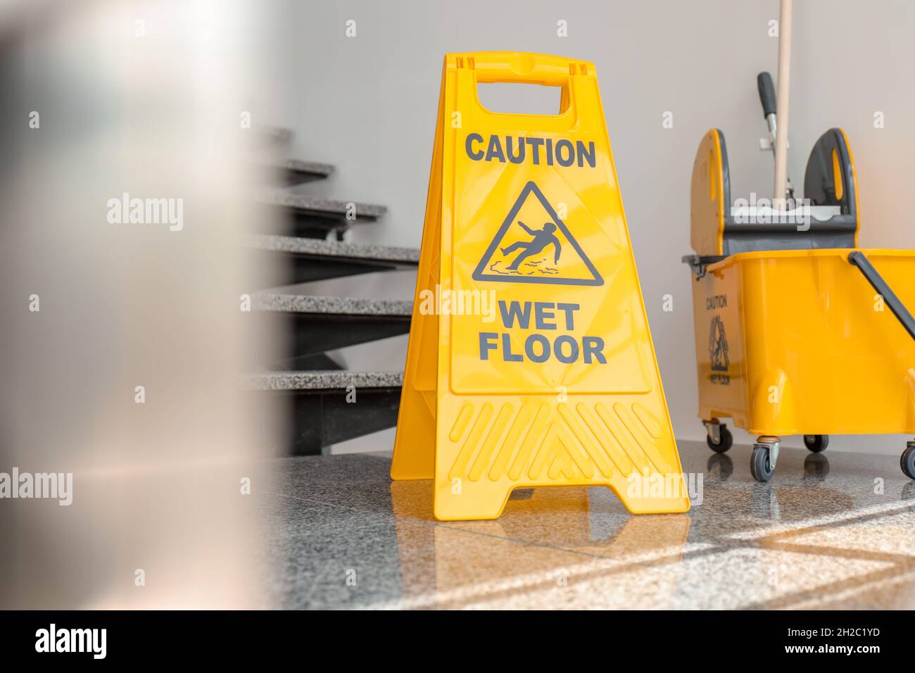 Safety sign with phrase Caution wet floor and mop bucket near stairs