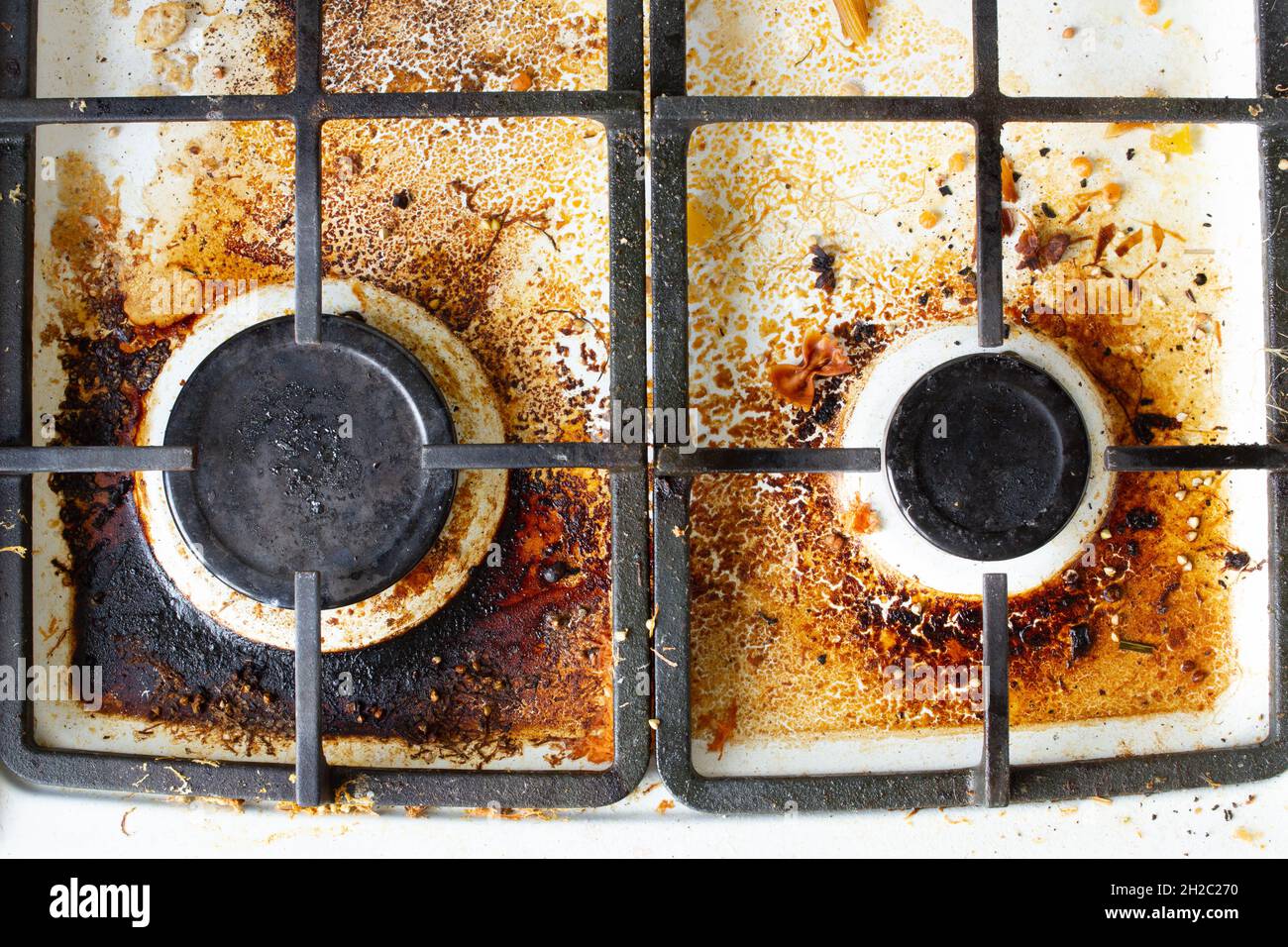 Dirty gas stove surface. Two gas burners and cast iron grate of a gas oven surrounded by old leftovers of food and drinks. Top area surface and burner Stock Photo