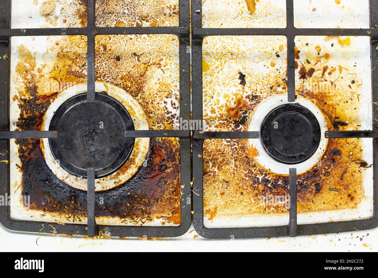 Dirty gas stove surface. Two gas burners and cast iron grate of a gas oven surrounded by old leftovers of food and drinks. Top area surface and burner Stock Photo