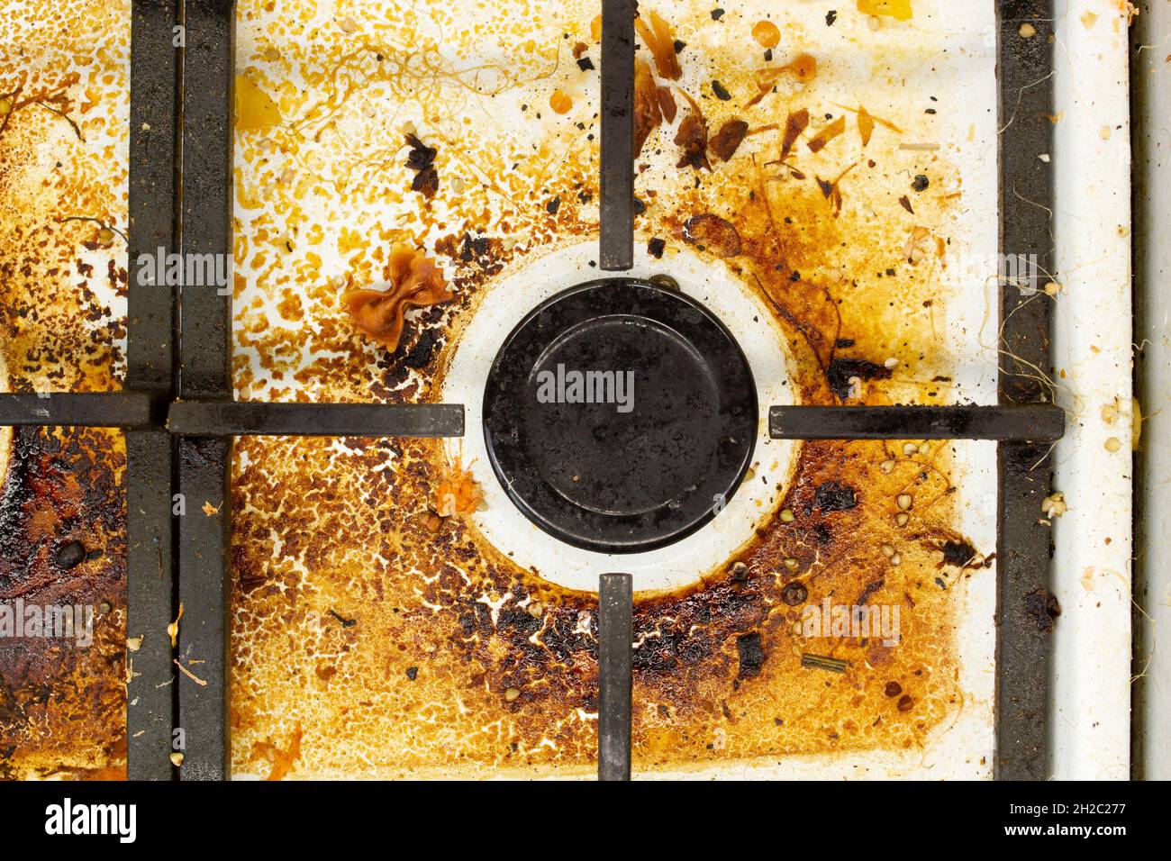 Dirty gas stove surface. Medium gas burner and cast iron grate of a gas oven surrounded by old leftovers of food and drinks. Top area surface Stock Photo